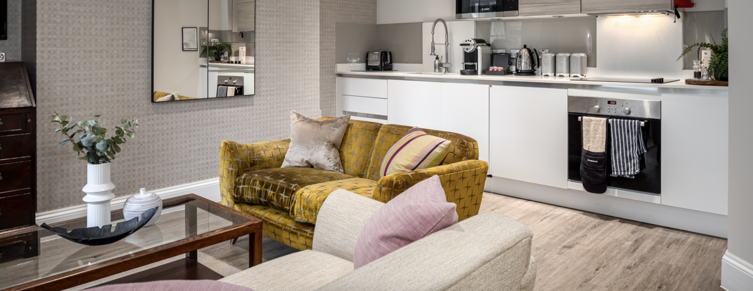 yellow velvet sofa with white kitchenette to the rear