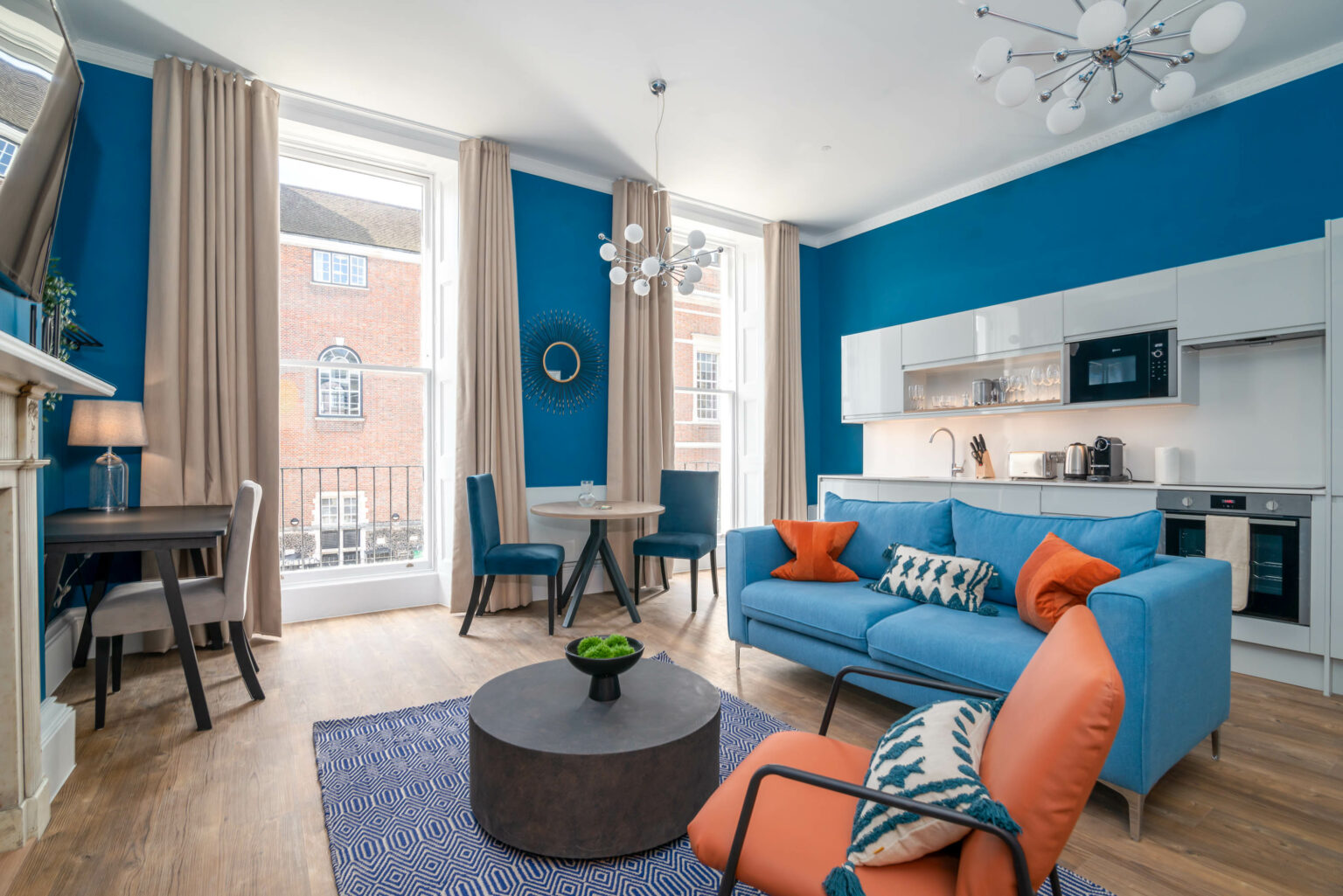 blue feature wall with kitchen and blue sofa in front with orange accent chair